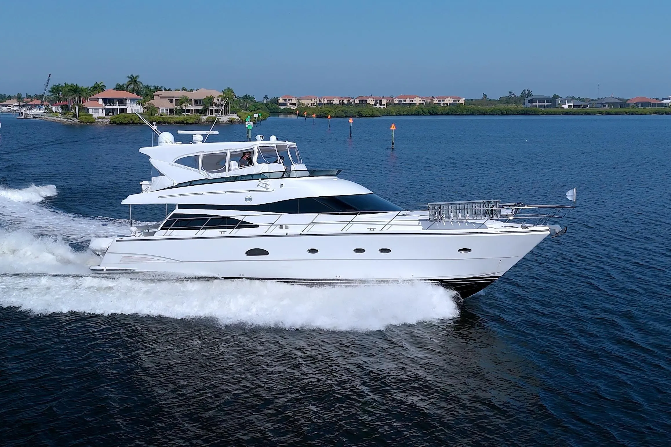 2005 Neptunus 62 Flybridge yacht cruising on a sunny day, near waterfront homes.