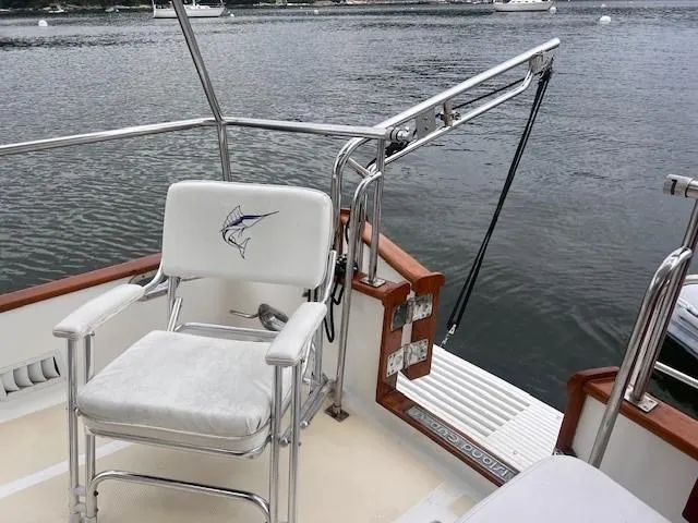 Emily Anne Yacht Photos Pics 2001 Island Gypsy Euro Sedan Trawler fishing chair with marlin logo, docked by calm waters.