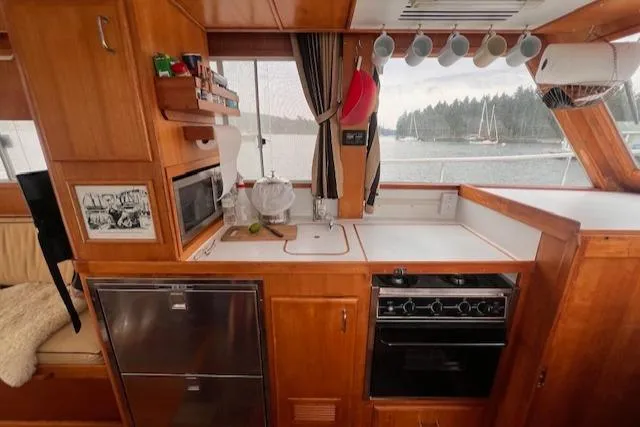 Emily Anne Yacht Photos Pics 2001 Island Gypsy Euro Sedan Trawler kitchen with wooden cabinetry, stove, and scenic window view.