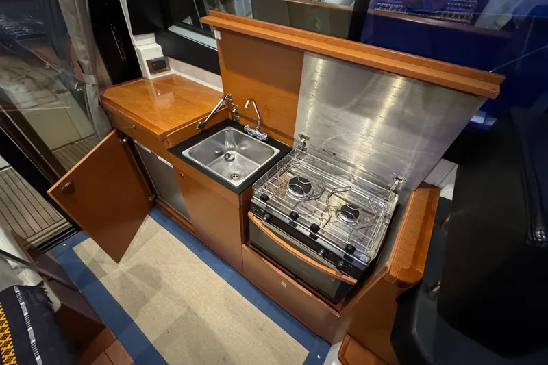  Yacht Photos Pics 2017 Jeanneau NC 9 yacht kitchen with stove, sink, and wooden cabinetry.