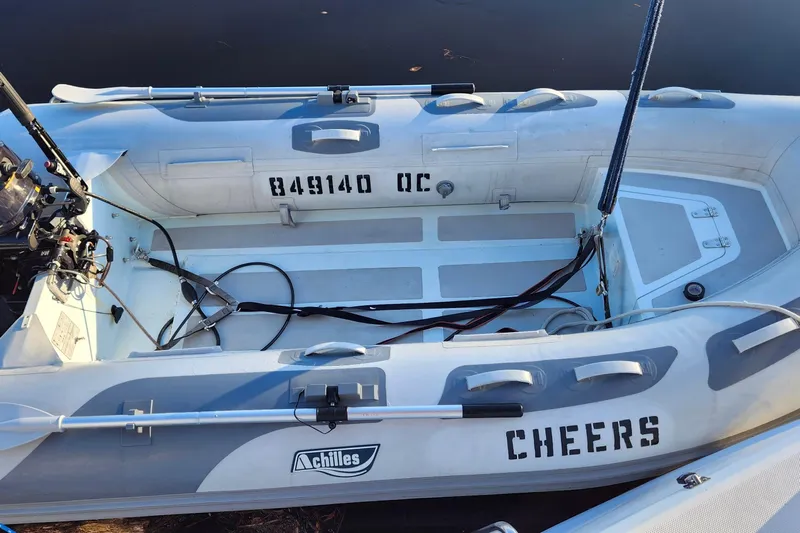 Free Range Yacht Photos Pics Inflatable boat with "Cheers" text, motor, and registration number, docked on calm water.