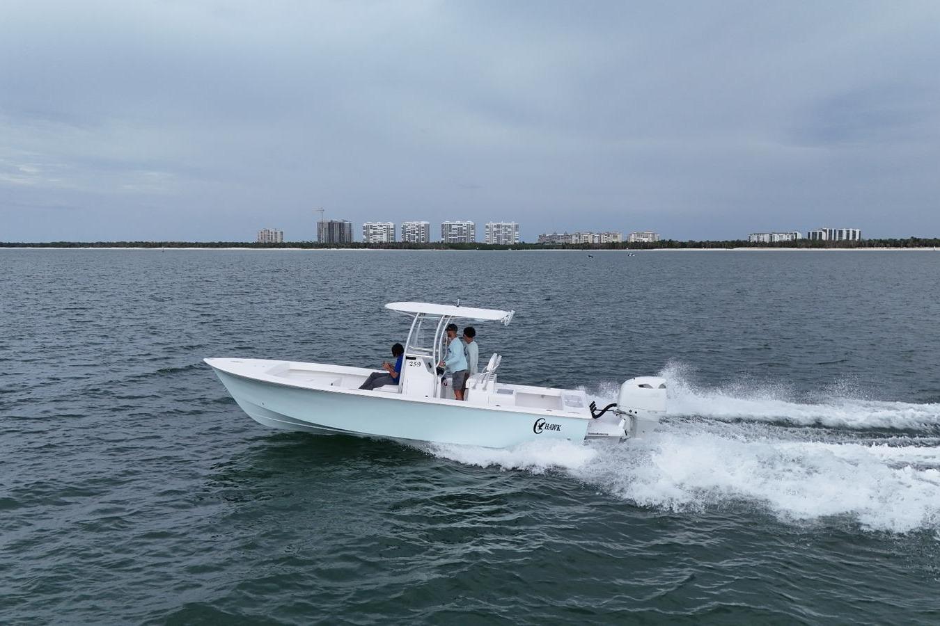 2026 C-Hawk 25 Center Console boat cruising on open water near a coastal cityscape.