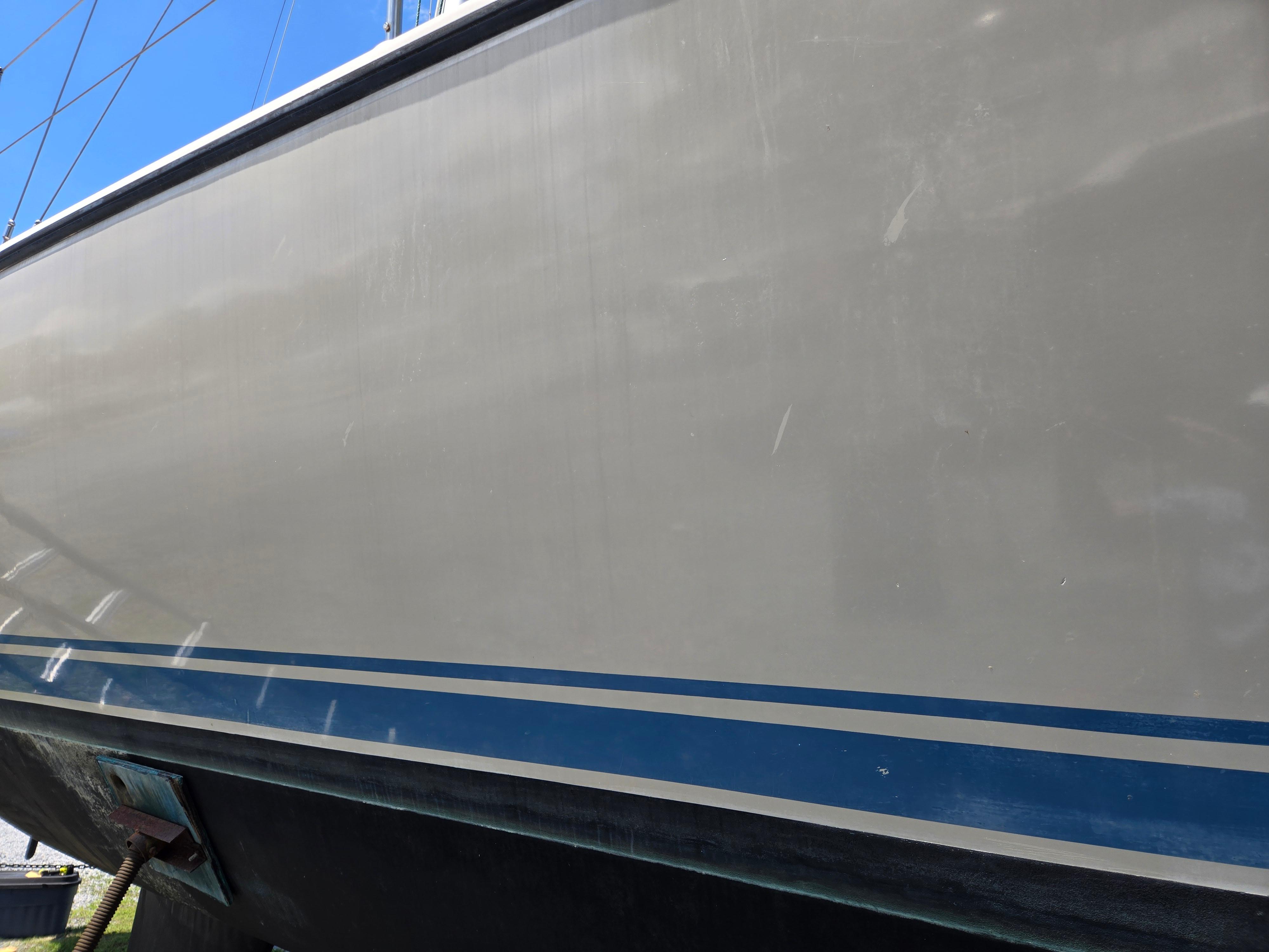 1987 Dehler Optima 34 sailboat hull with blue stripes, docked under clear sky.