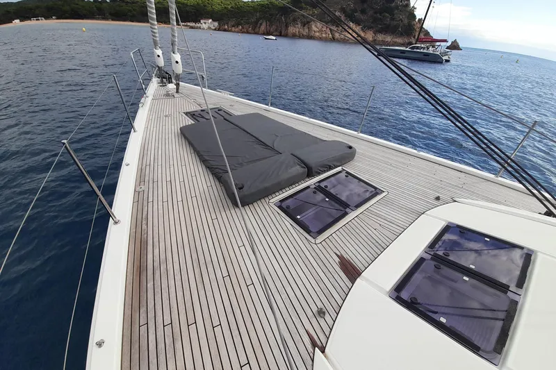  Yacht Photos Pics Deck of 2015 Jeanneau Yachts 64 with sunbathing area, anchored near scenic coastline.