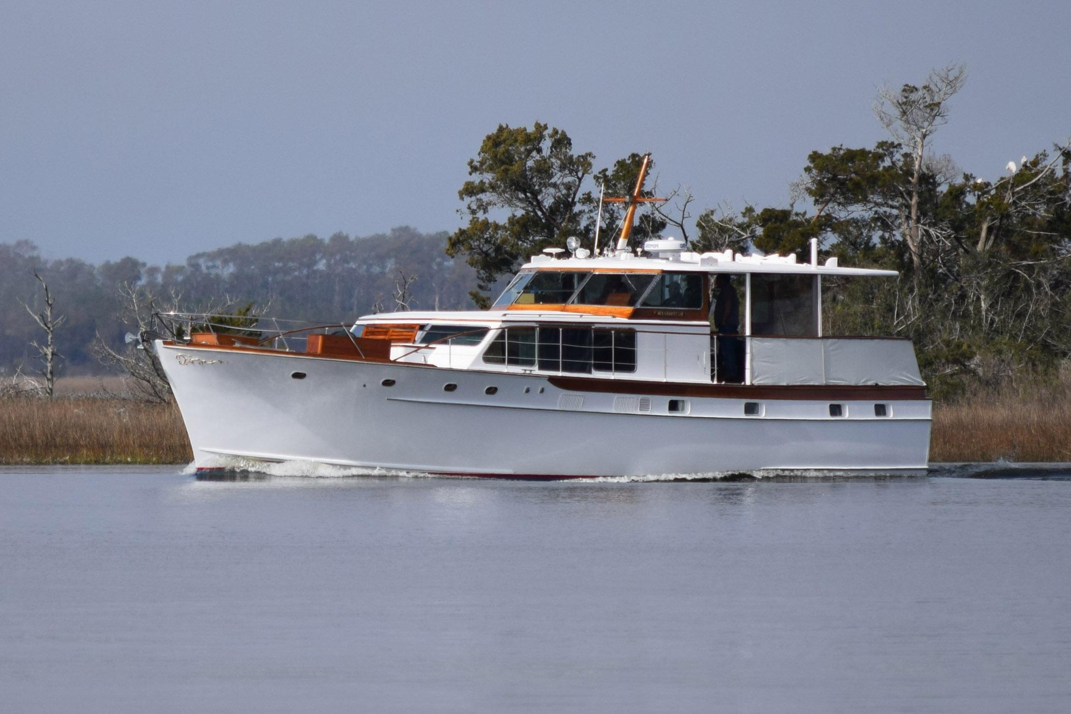 Classic 1966 Trumpy 55 yacht cruising on calm waters, surrounded by trees.