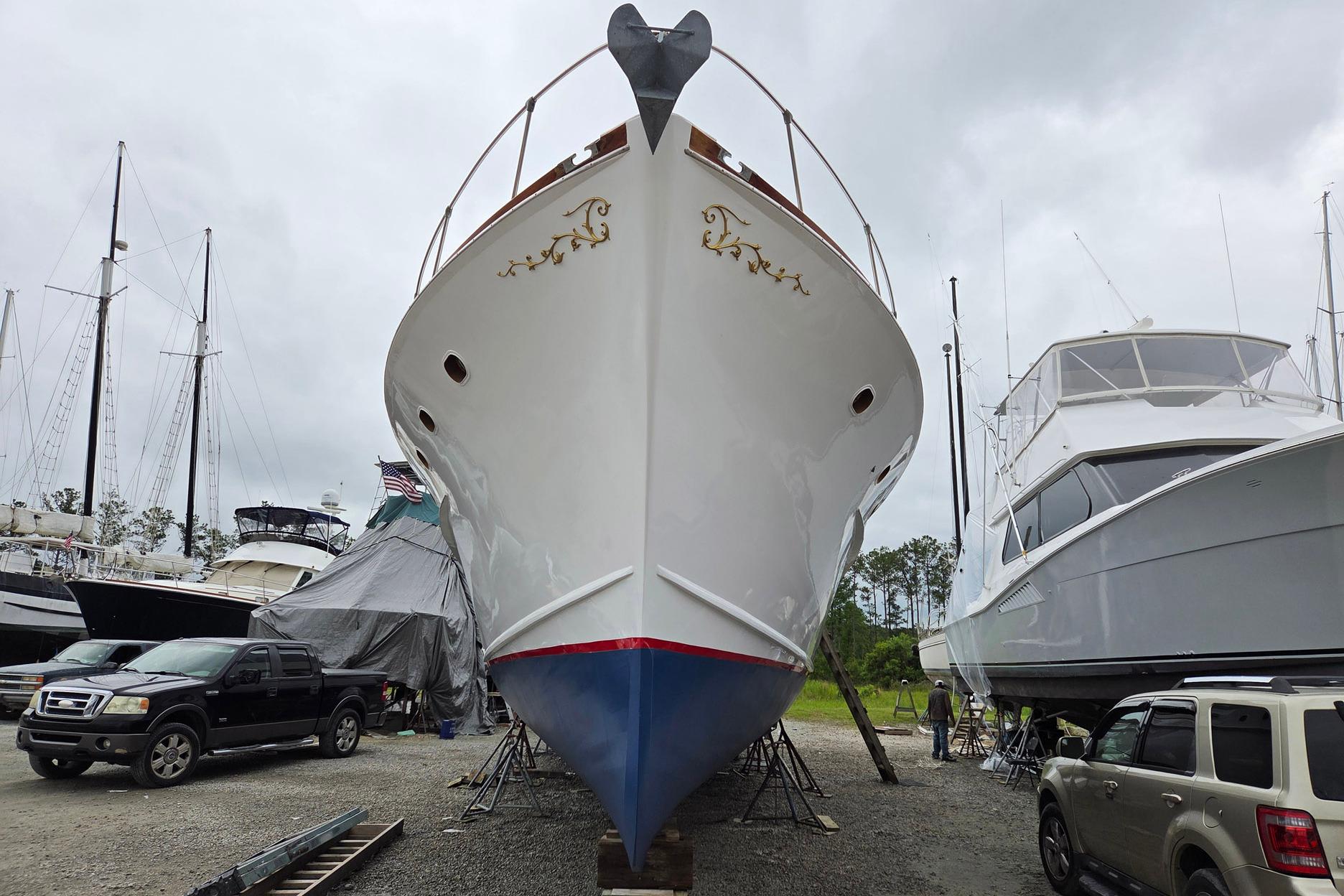 1966 Trumpy 55 yacht in dry dock, surrounded by other boats and vehicles.