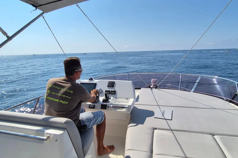  Yacht Photos Pics Man steering a 2022 Prestige 460 yacht on open sea under clear blue sky.