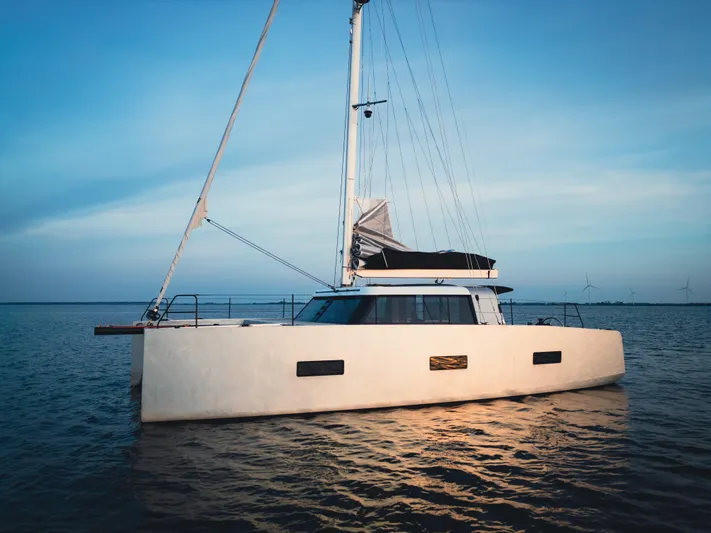  Yacht Photos Pics Sleek 2025 Vaan R4 catamaran sailing on calm waters at sunset.