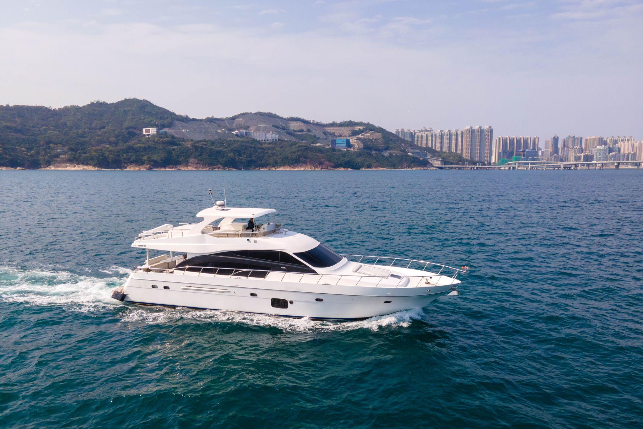 Luxurious 2011 Ruby 68 yacht cruising near coastal cityscape and scenic hills.