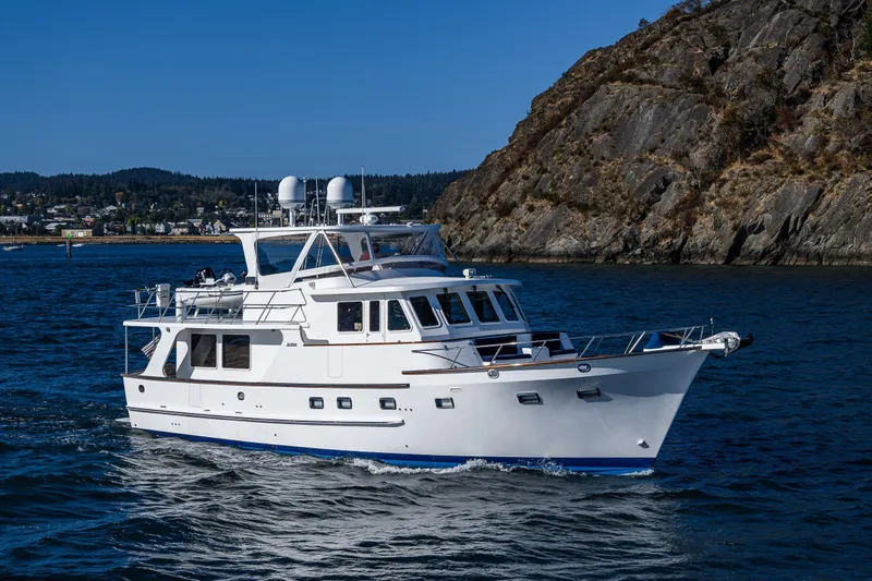 Flyin Low Yacht Photos Pics 2007 DeFever 56 yacht cruising near rocky coastline under clear blue sky.