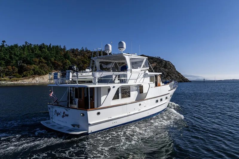 Flyin Low Yacht Photos Pics 2007 DeFever 56 yacht cruising near rocky coastline under clear blue sky.