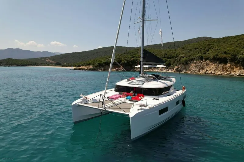  Yacht Photos Pics 2021 Lagoon 46 catamaran anchored in a serene bay with clear blue water.