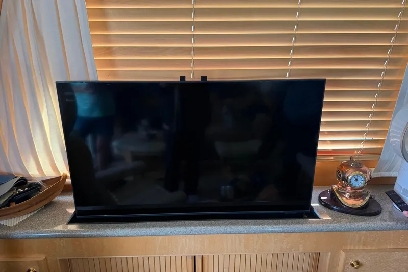 Gabbiano Yacht Photos Pics Flat-screen TV on a wooden cabinet with blinds and a decorative clock nearby.