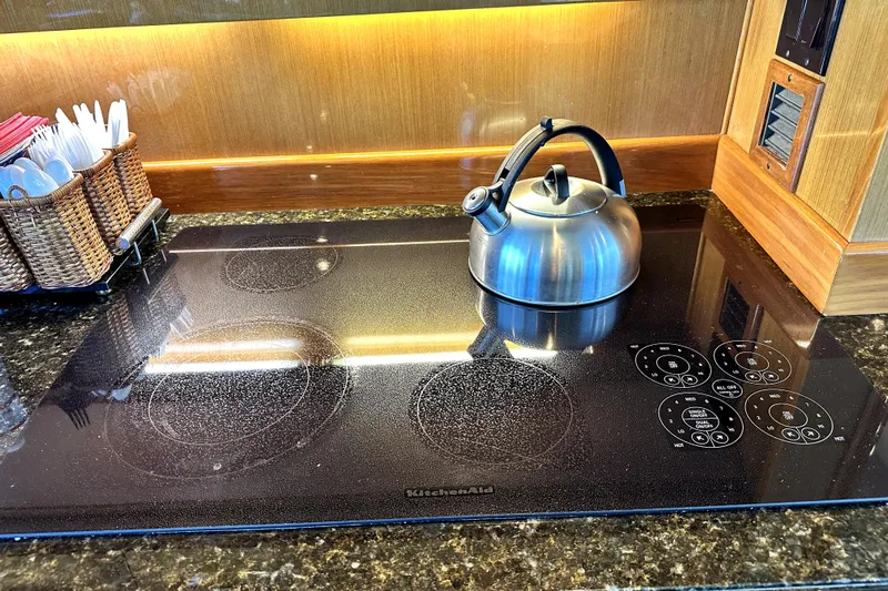Reel Inn Yacht Photos Pics Modern kitchen with a sleek black cooktop, stainless steel kettle, and utensil basket.