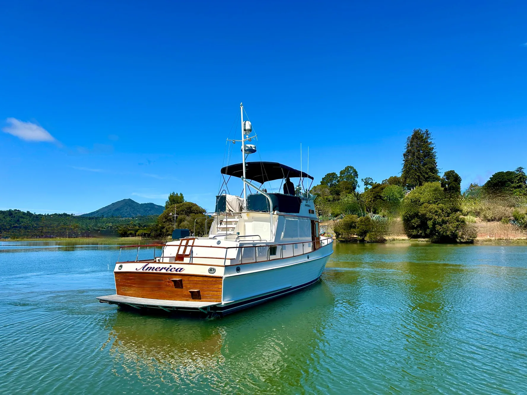 1989 Grand Banks 42 Classic yacht on serene water with lush greenery backdrop.