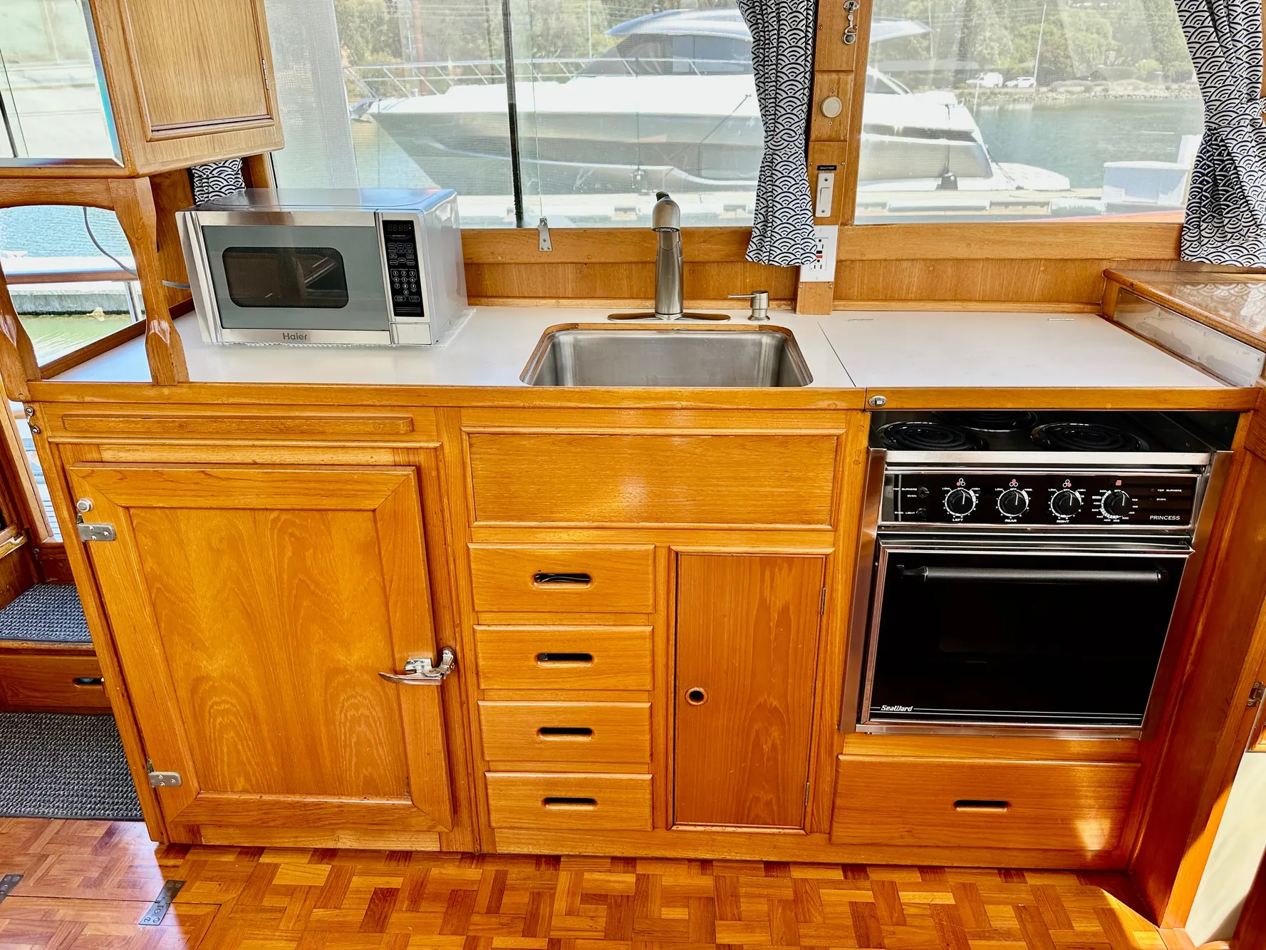 Wooden kitchen interior of 1989 Grand Banks 42 Classic yacht with stove, sink, and microwave.