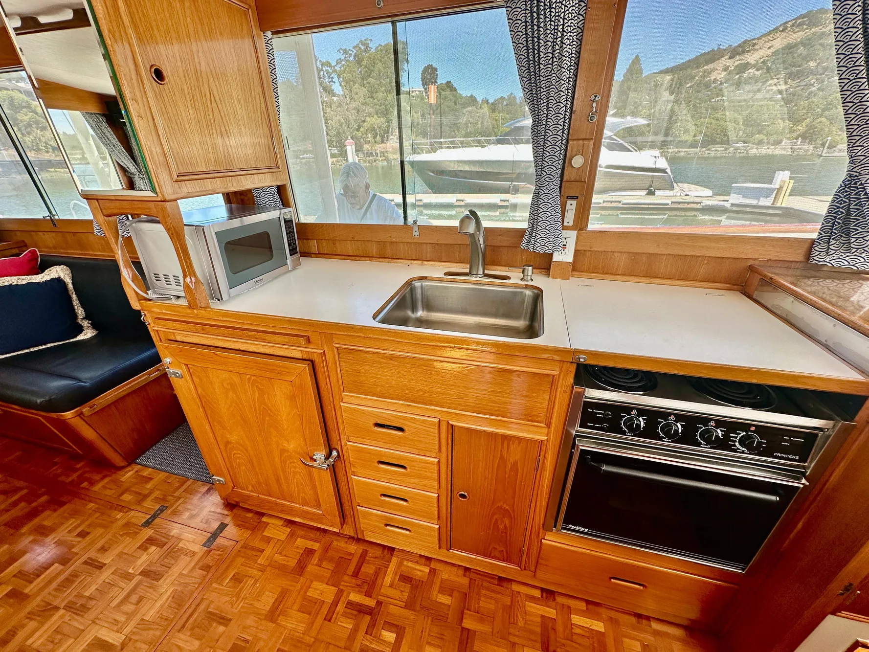 1989 Grand Banks 42 Classic yacht kitchen with wood cabinetry, sink, stove, and microwave.