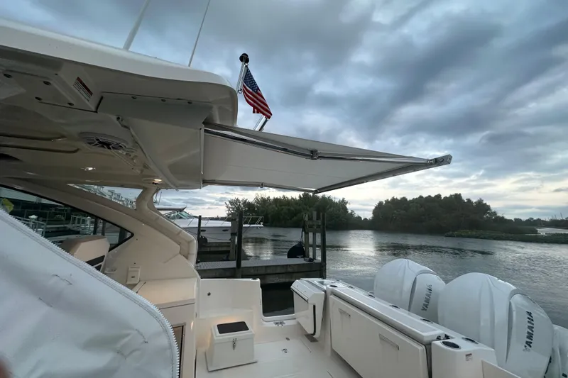  Yacht Photos Pics 2023 Pursuit DC 326 Dual Console boat docked by a serene river under cloudy skies.