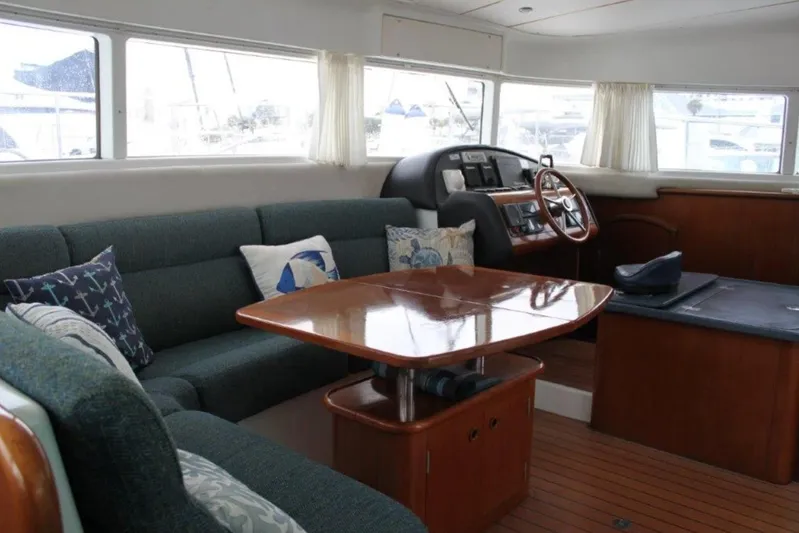 Mangata Yacht Photos Pics Interior of 2003 Lagoon Power 43 yacht with wooden table, cushioned seating, and helm station.