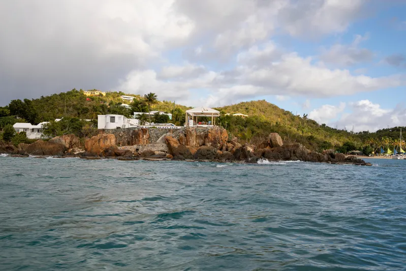  Yacht Photos Pics Coastal landscape with rocky shoreline, lush greenery, and scattered buildings under a partly cloudy sky.