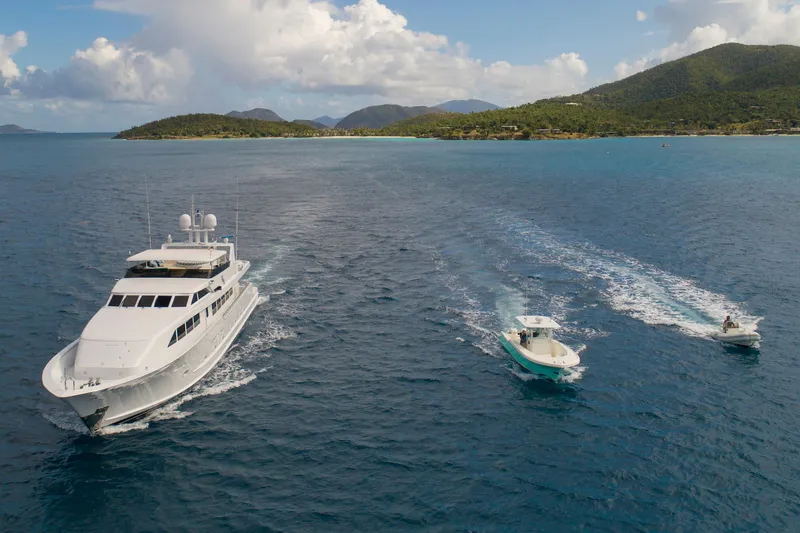  Yacht Photos Pics Luxury yacht Broward Marine Raised Pilothouse 1994 cruising with smaller boats in scenic ocean.