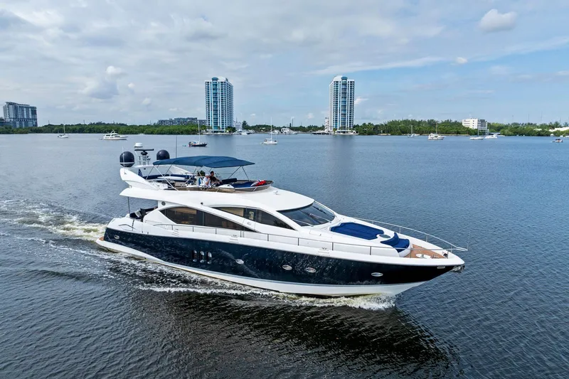 Persistence Yacht Photos Pics Luxurious 2006 Sunseeker 75 Yacht cruising on a serene waterway with cityscape backdrop.