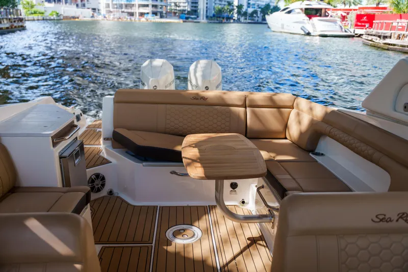  Yacht Photos Pics Luxurious Sea Ray boat interior with tan seating and wooden table on a sunny waterfront.