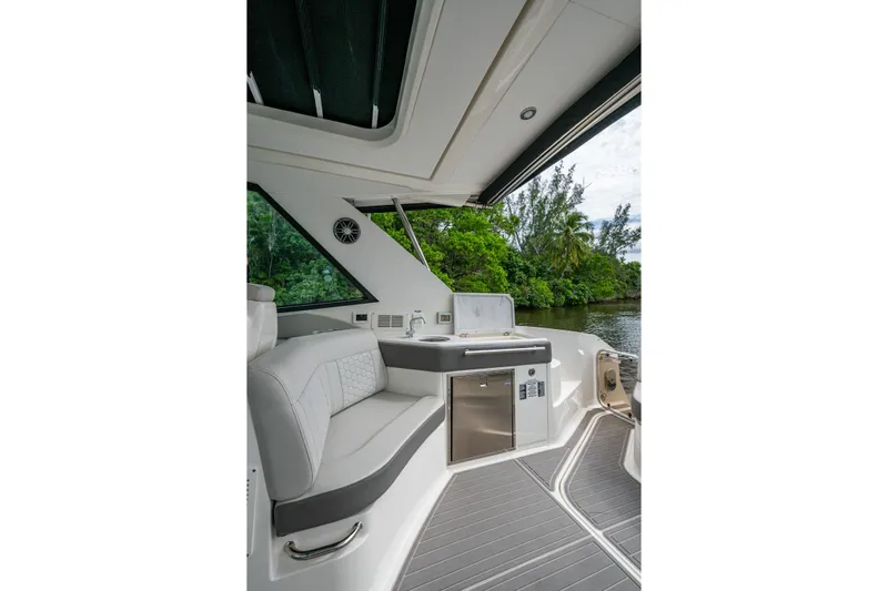  Yacht Photos Pics 2023 Sea Ray Sundancer 320 Outboard interior with seating and kitchenette, near lush greenery.
