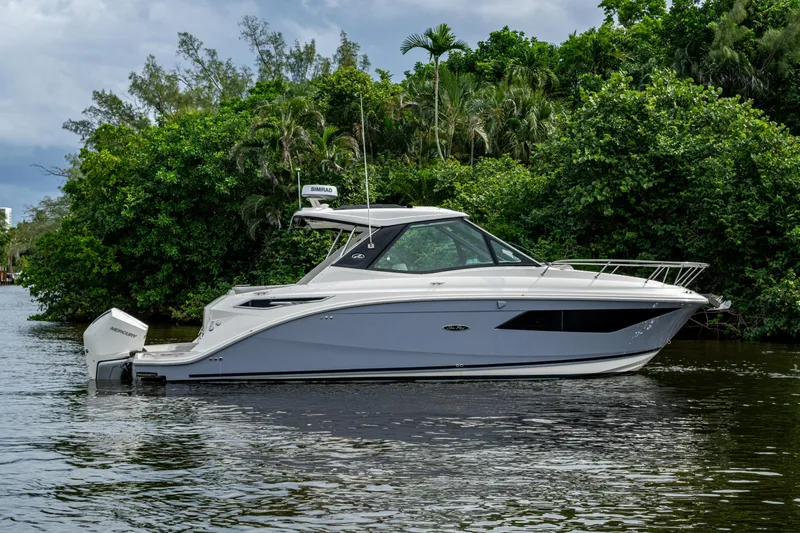  Yacht Photos Pics 2023 Sea Ray Sundancer 320 Outboard boat on calm water, surrounded by lush greenery.