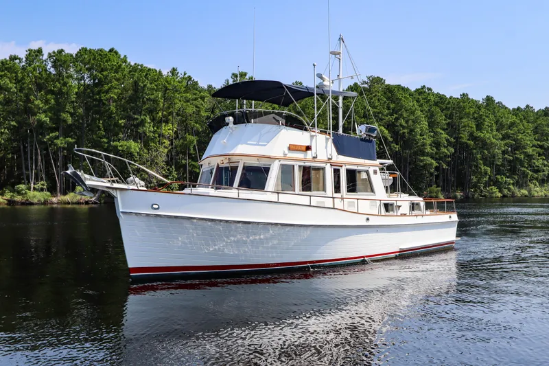 Tallulah Yacht Photos Pics 1989 Grand Banks 42 Classic yacht cruising on a serene river with lush green forest backdrop.