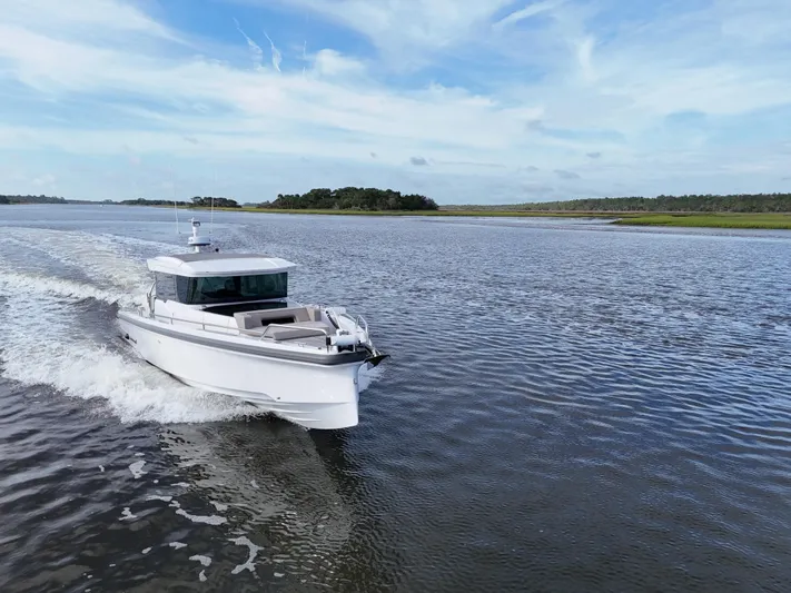  Yacht Photos Pics 2023 Axopar 37 Cross Cabin cruising on a serene waterway under a clear blue sky.