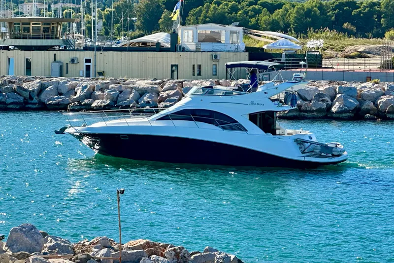 Motomar 1 Yacht Photos Pics 2008 Sea Ray 500 Sedan Bridge yacht cruising near rocky shoreline.