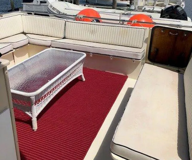 The Bottom Line Yacht Photos Pics 1987 Hatteras Flybridge yacht interior with cushioned seating, glass table, and red carpet.