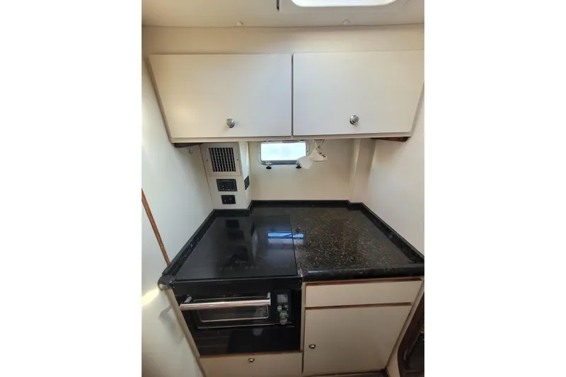 Ki Zen Yacht Photos Pics Compact kitchen area in a 1995 Lagoon TPI boat with black countertop and white cabinets.