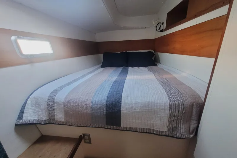 Ki Zen Yacht Photos Pics Cozy cabin bedroom in 1995 Lagoon TPI boat with striped bedding and wooden accents.