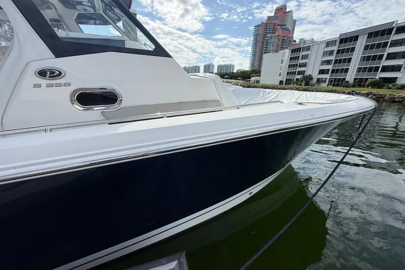 Alroma Yacht Photos Pics 2022 Pursuit S 358 Sport boat docked near waterfront buildings under a cloudy sky.