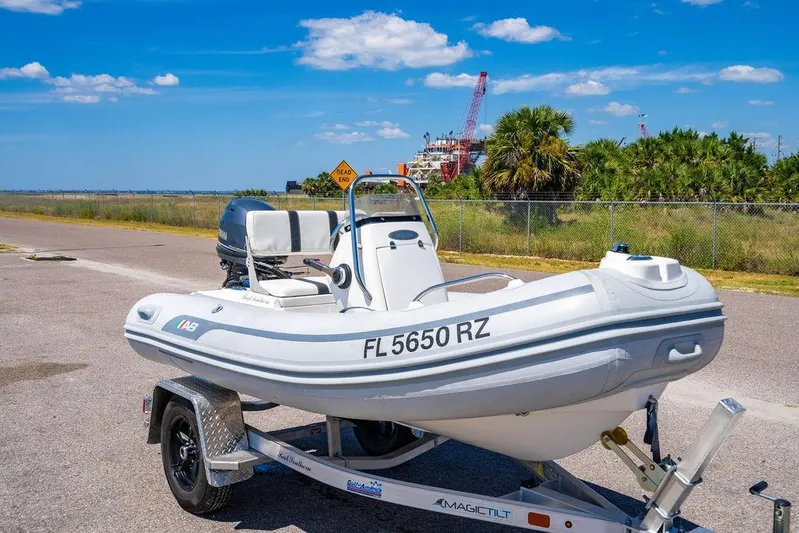 Reel Southern Yacht Photos Pics White inflatable boat on trailer, parked near a road with palm trees and cranes in the background.