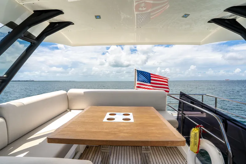 Soiral Yacht Photos Pics Luxurious 2023 Prestige 520 yacht deck with seating, table, and American flag on open sea.