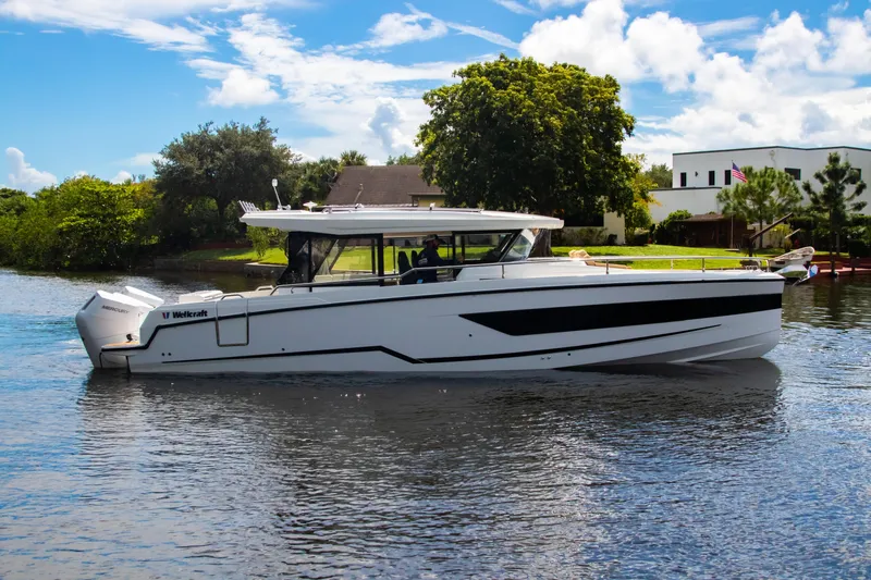  Yacht Photos Pics 2025 Wellcraft 38 Explorer boat cruising on a sunny day, surrounded by lush greenery.