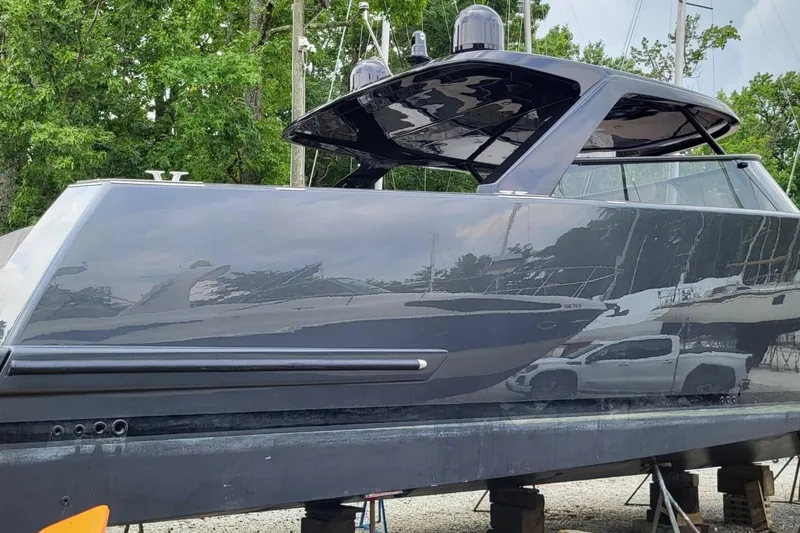  Yacht Photos Pics 2023 VanDutch 56 yacht in dry dock, sleek black design, surrounded by trees and equipment.