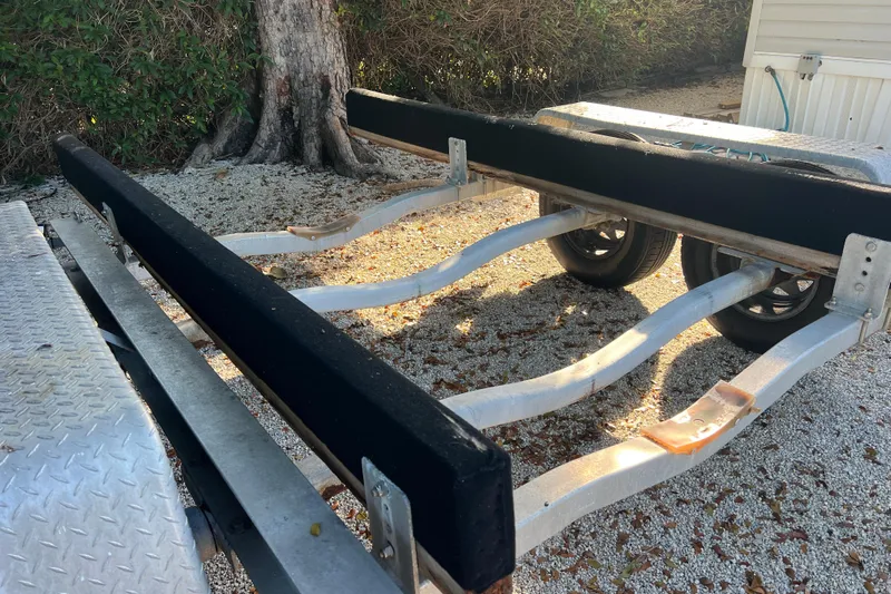  Yacht Photos Pics Boat trailer for 2003 Contender 27 Open, parked on gravel near a tree.