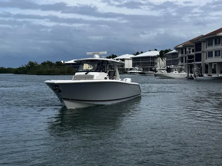  Yacht Photos Pics 2024 Pursuit 358 SPORT boat cruising near waterfront homes under cloudy skies.