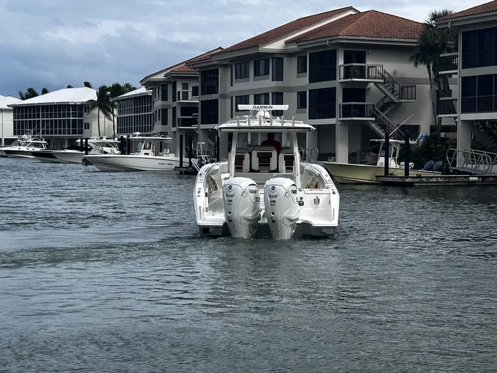  Yacht Photos Pics 2024 Pursuit 358 SPORT boat navigating a marina with waterfront buildings.