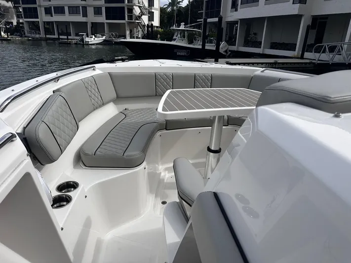  Yacht Photos Pics 2024 Pursuit 358 SPORT boat interior with gray seating and table, docked near waterfront buildings.