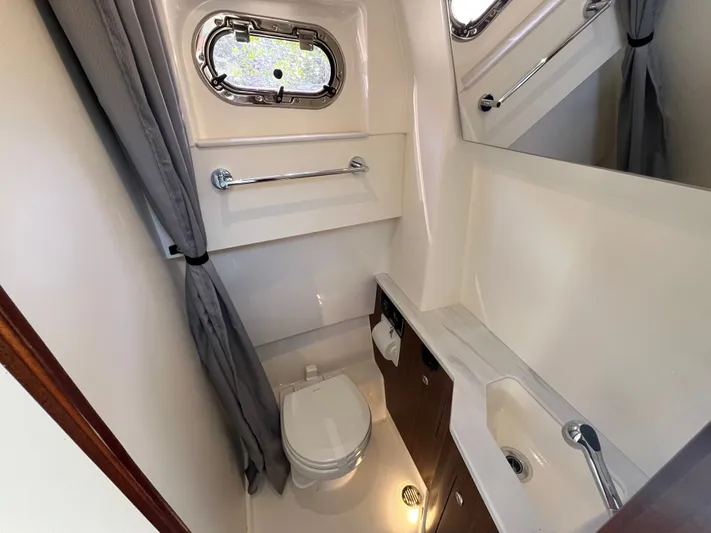  Yacht Photos Pics 2024 Pursuit 358 SPORT boat bathroom with toilet, sink, mirror, and porthole window.
