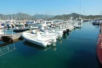 Boats docked in a marina with mountains in the background, clear blue sky.