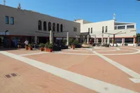 Modern plaza with beige buildings, outdoor seating, and clear blue sky.