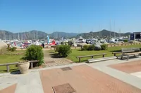 Scenic marina view with boats, lush greenery, and distant mountains under a clear blue sky.