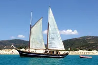 Vintage 1944 Custom Schooner 22 m sailing near a scenic coastline with clear blue water.