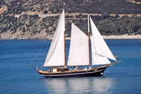 Vintage 1944 Custom Schooner 22 m sailing in serene blue waters near a rocky coastline.